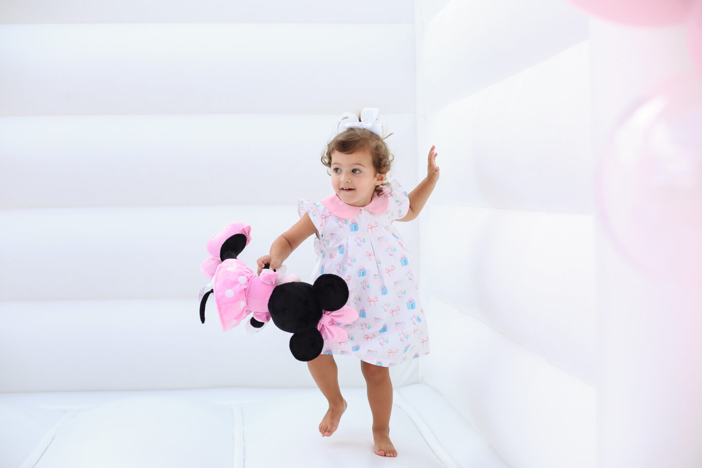 little girl in dress holding Minnie Mouse inside a white bounce house