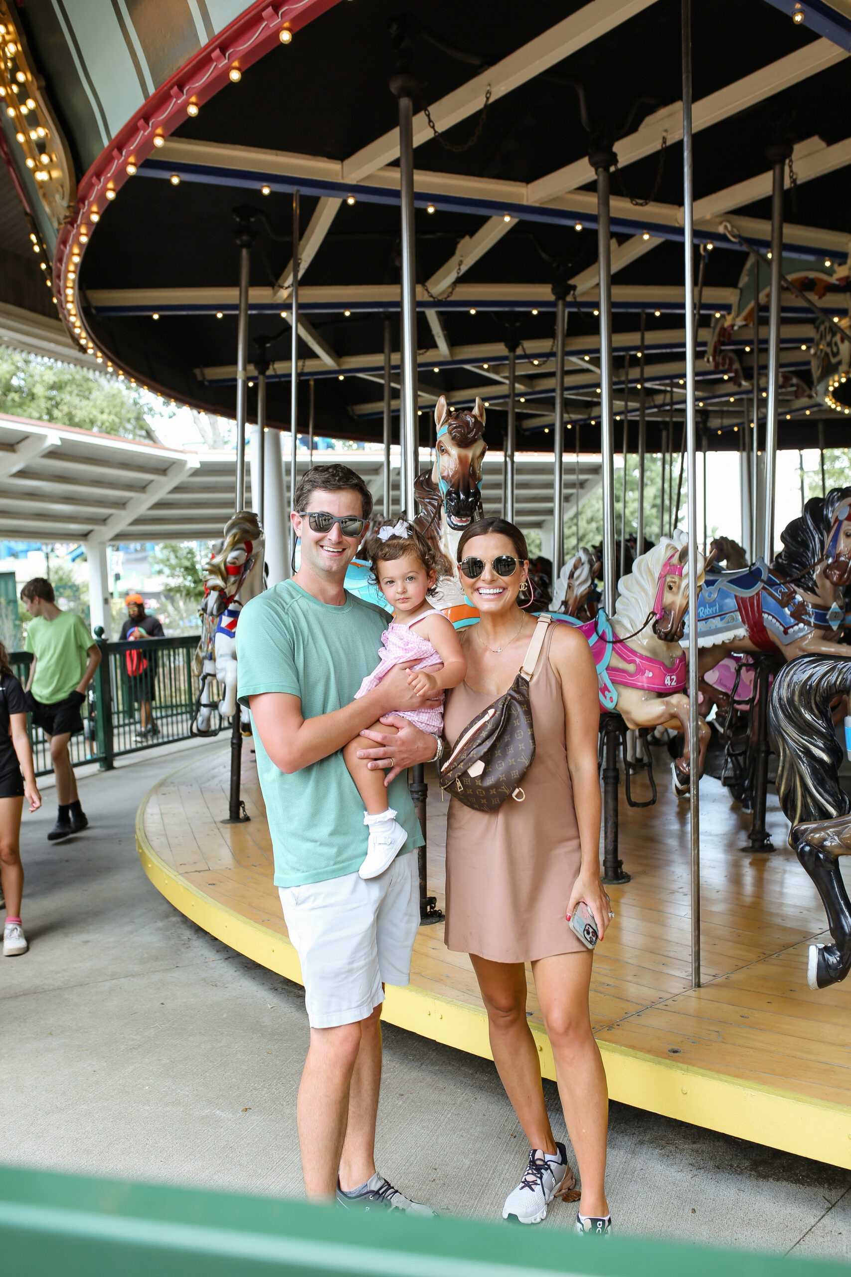 woman man and toddler in front of carousel at amusement park
