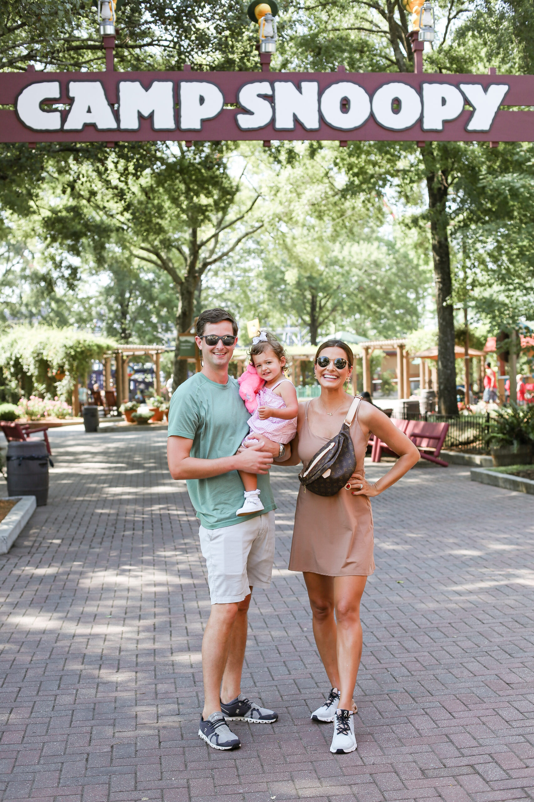 man woman and toddler in front of a sign that says Camp Snoopy