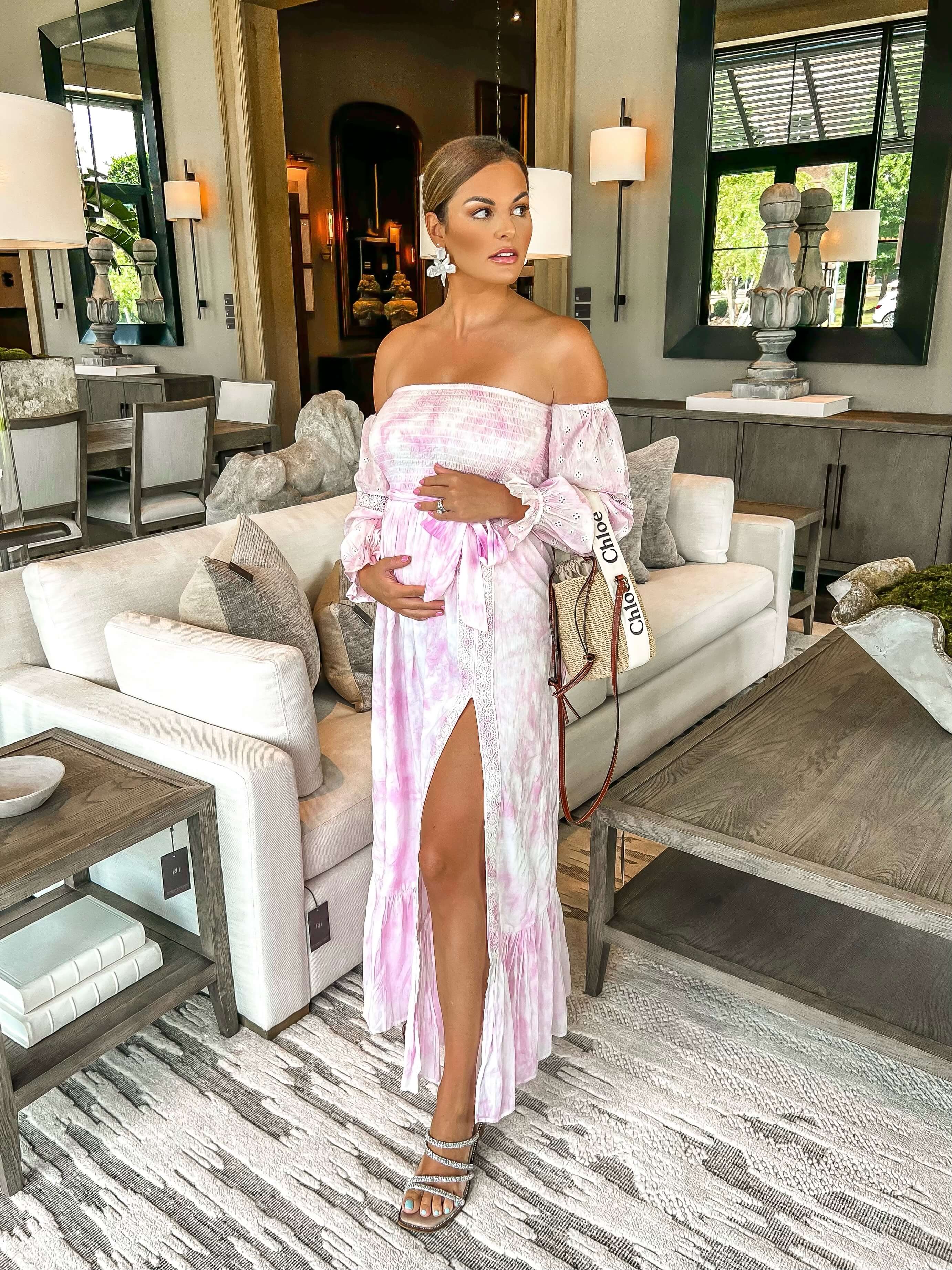 woman standing in pink off the shoulder dress in front of white sofa