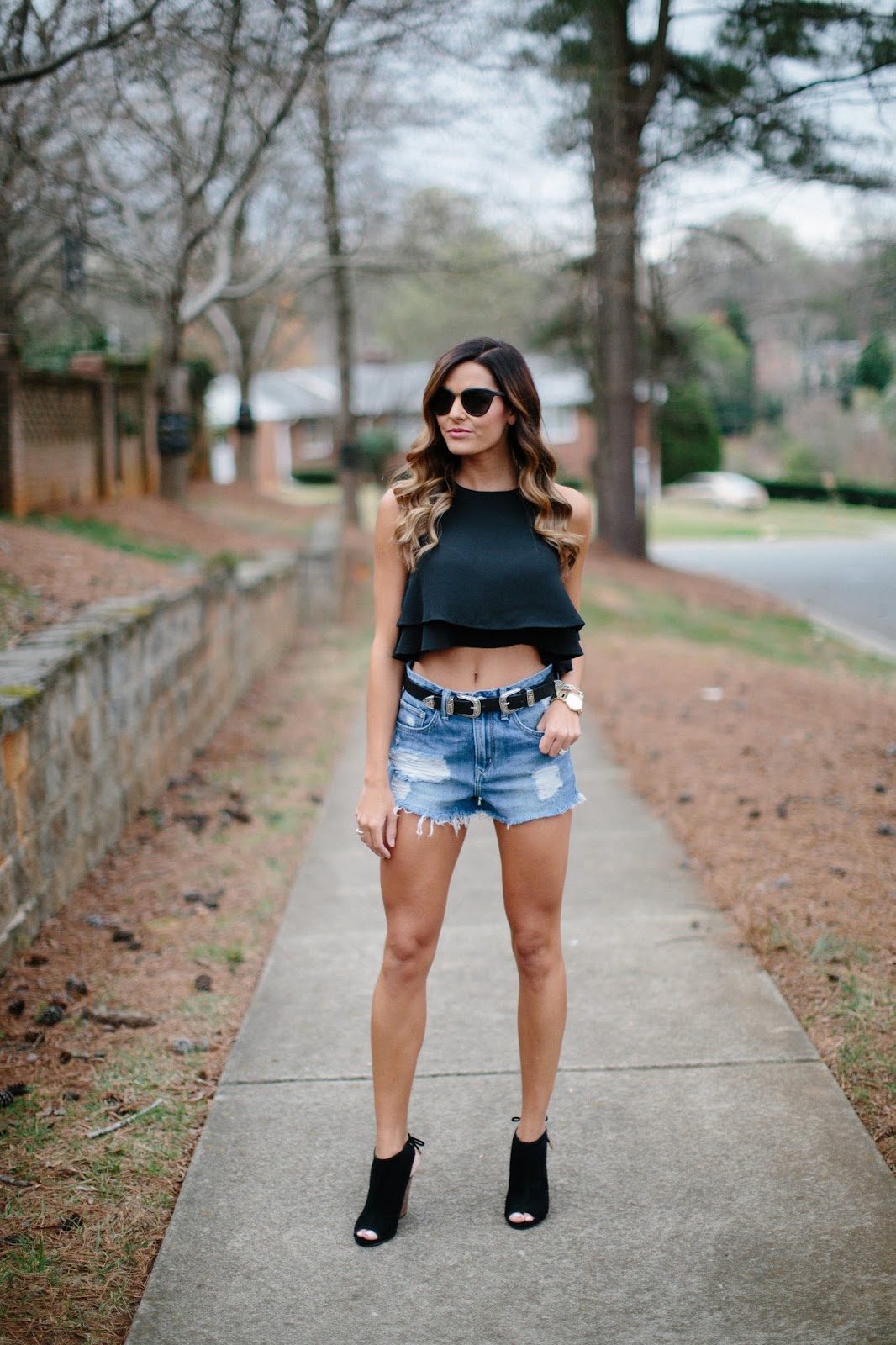 woman standing on sidewalk wearing denim shorts and black ankle boots