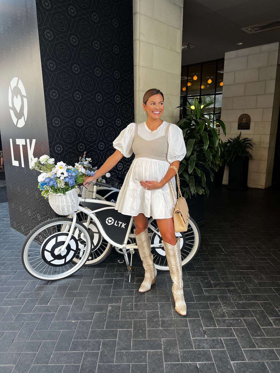 girl in white dress standing in front of white bicycle with blue flowers in the basket at LTK conference 2022