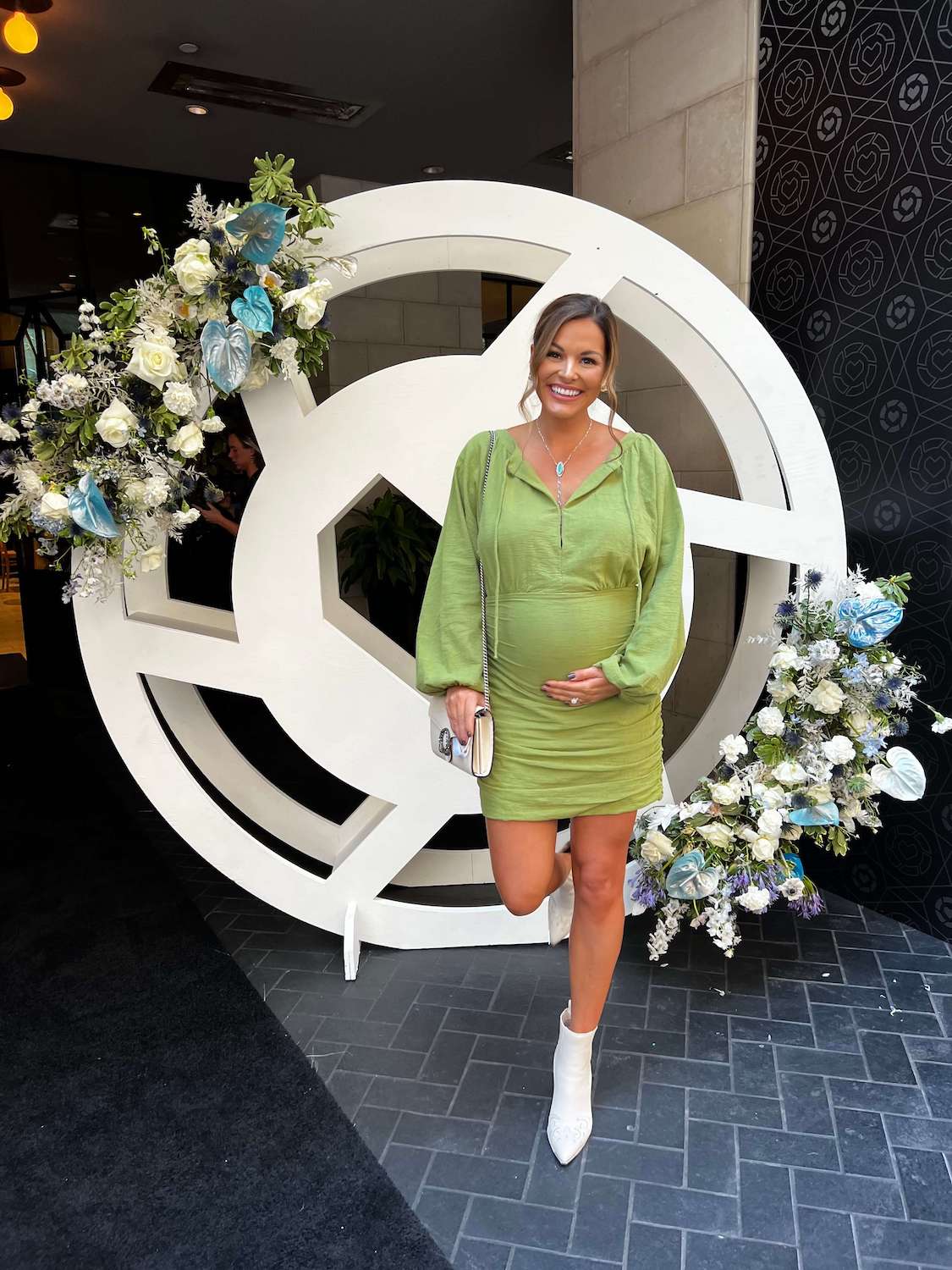 woman in green dress holding baby belly with white boots