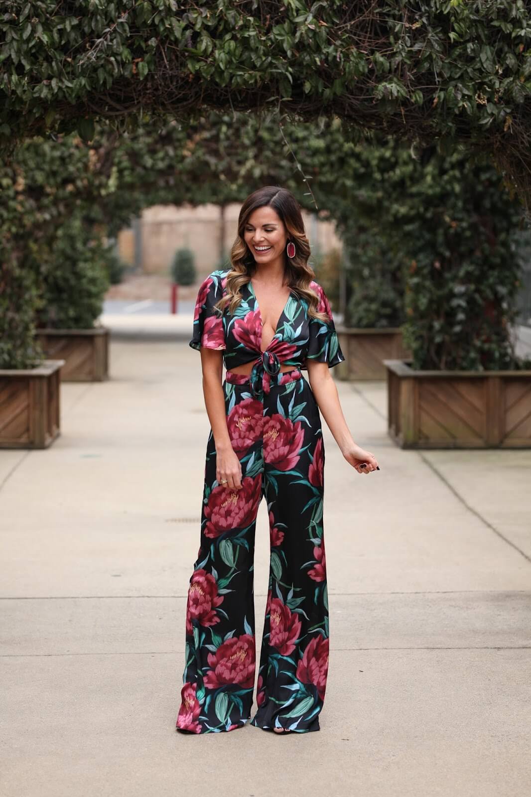 woman in floral jumpsuit in front of arch of greenery