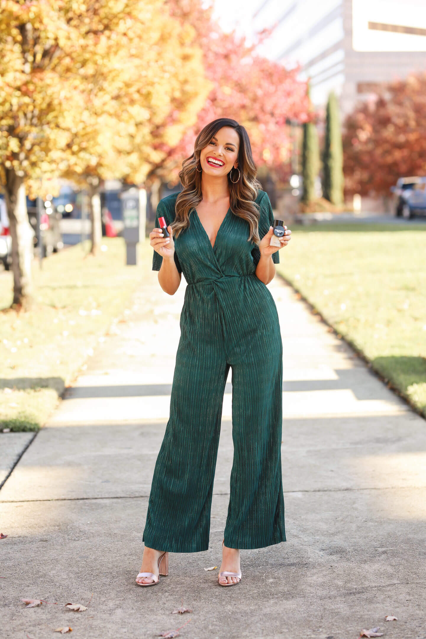 woman in green sparkly jumpsuit holding makeup in her hands