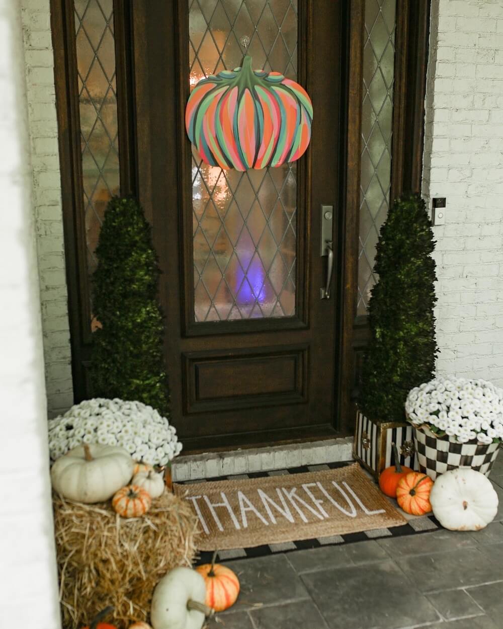 front porch with pumpkin door hanger and pumpkins around the base of the door