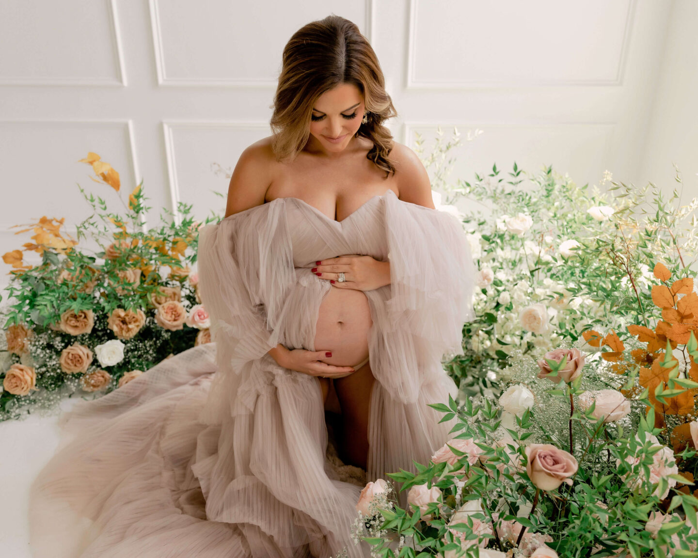woman on her knees with flowers around her with flowy maternity dress