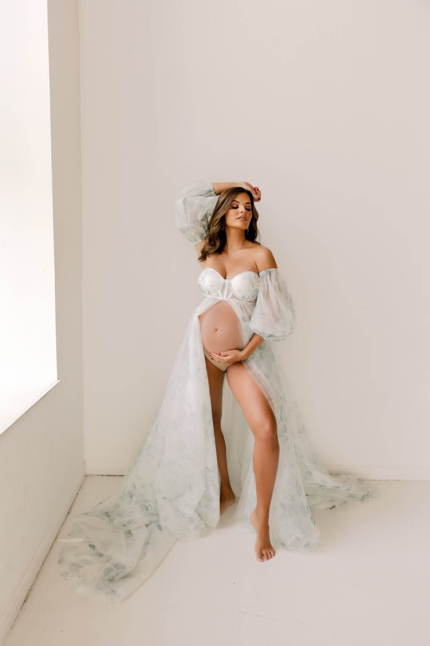 woman standing in front of white background at maternity photoshoot with flowy dress