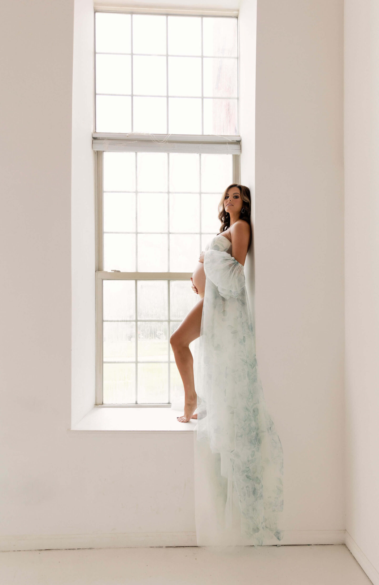 woman standing in window with flowy off the shoulder maternity dress