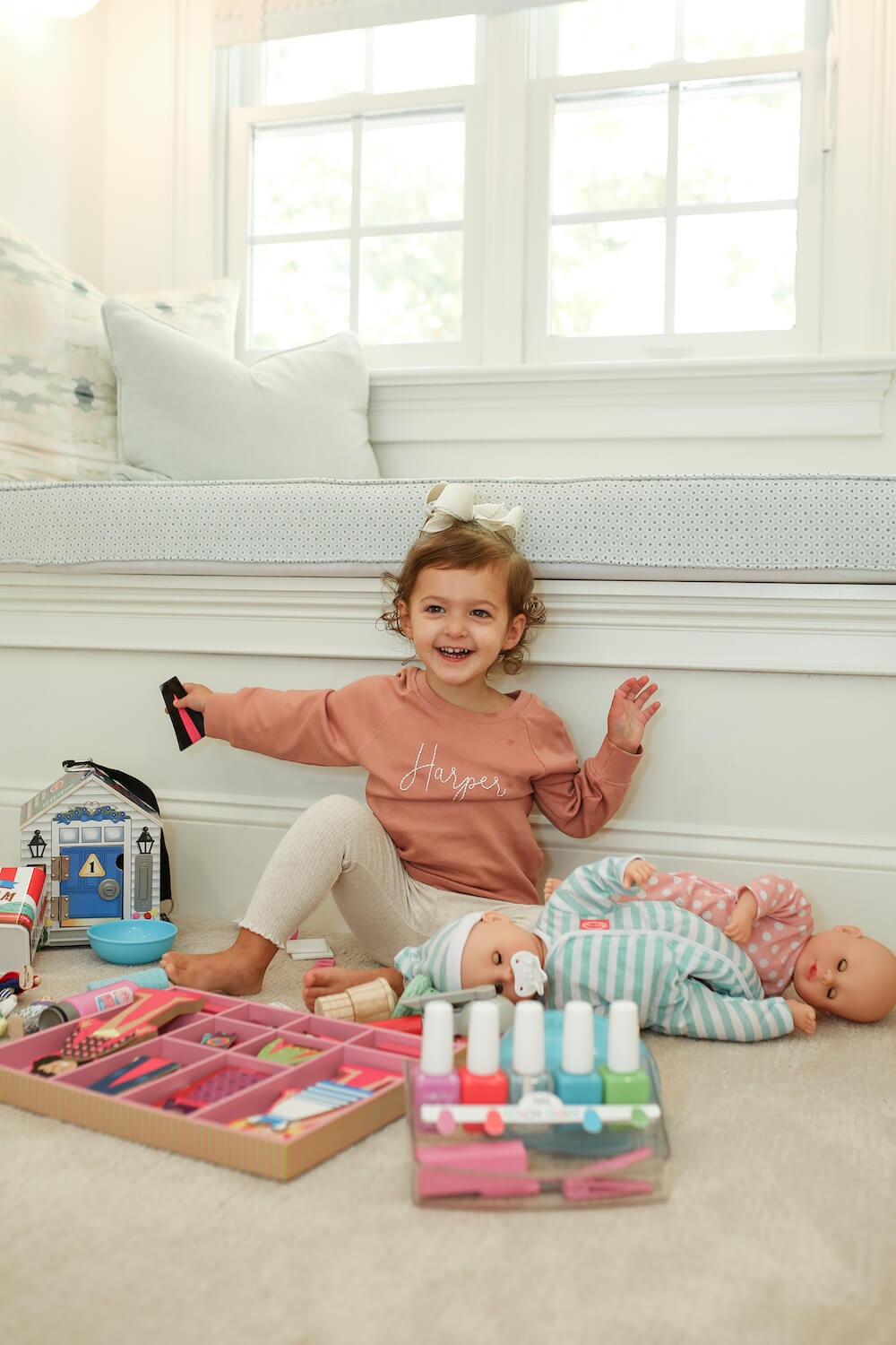 little girl playing with melissa and doug toys on the floor with mauve sweatshirt with her name on it