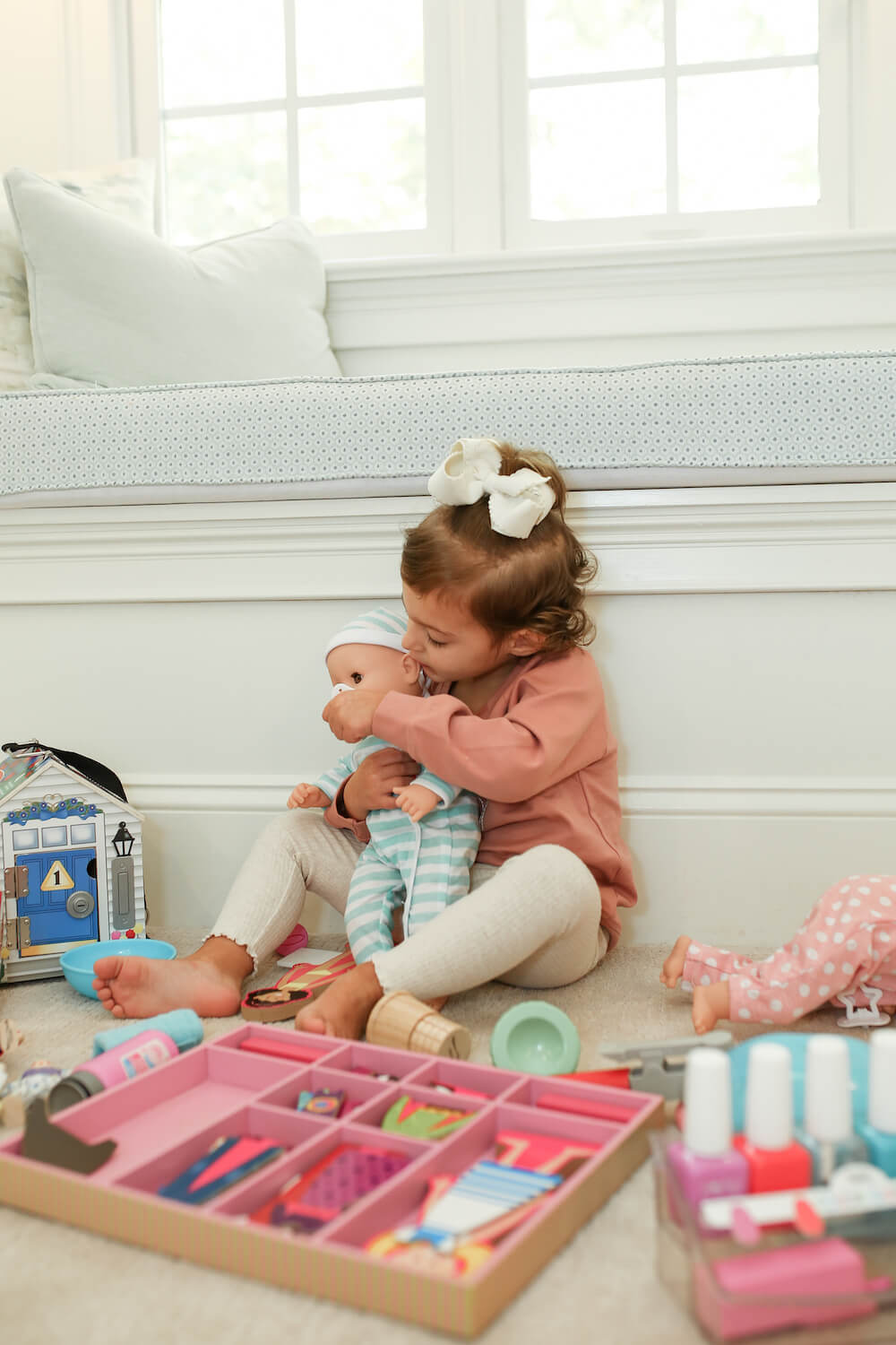 little girl playing with melissa and doug toys on the floor hugging baby