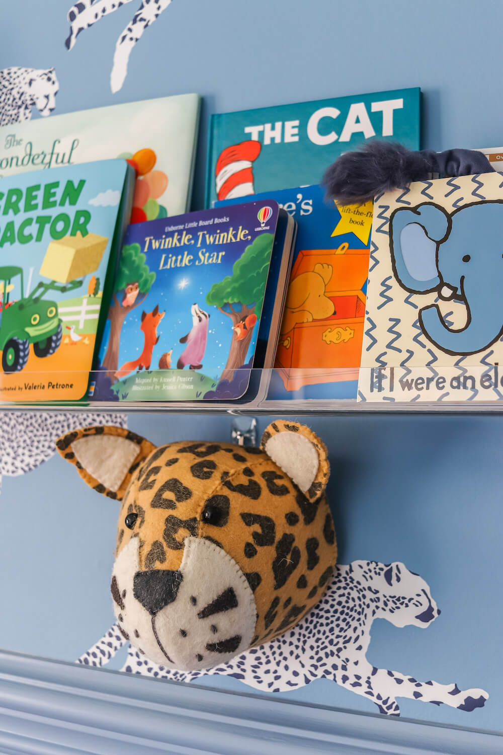 closeup of acrylic shelves with books in adventure themed nursery with leopard wallpaper