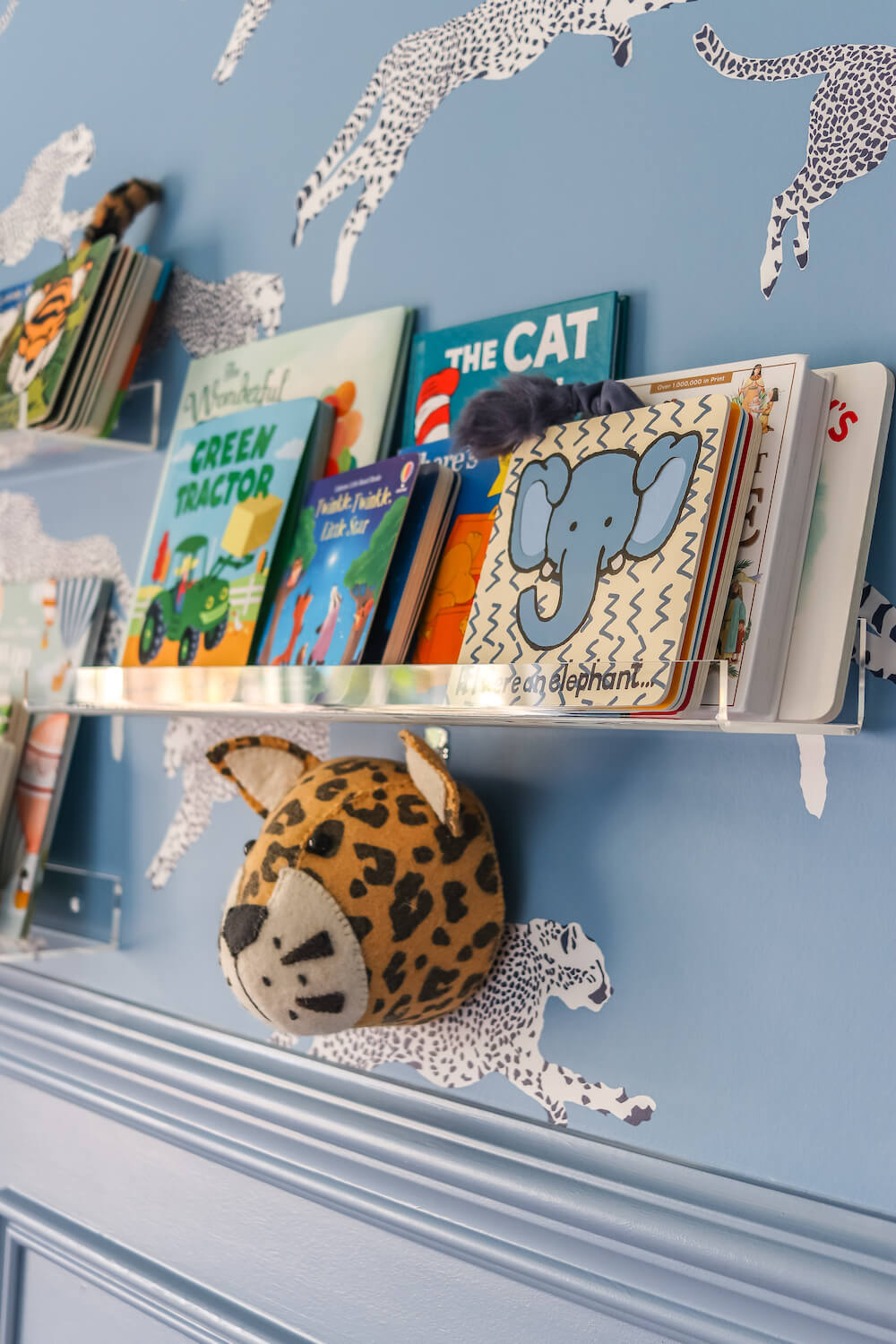 closeup of acrylic shelves with books in adventure themed nursery with leopard wallpaper