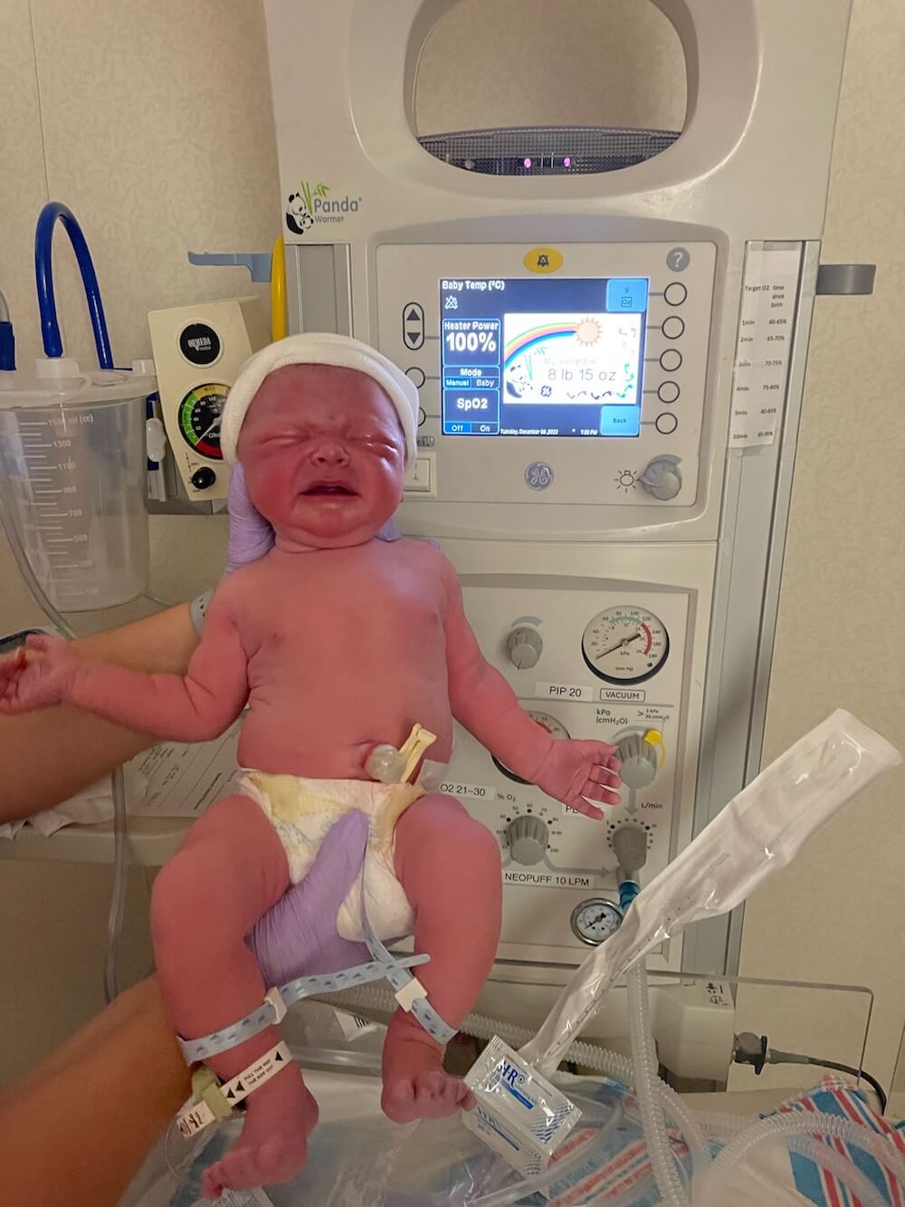 baby boy in diaper being held in front of sign that tells his length and weight at birth