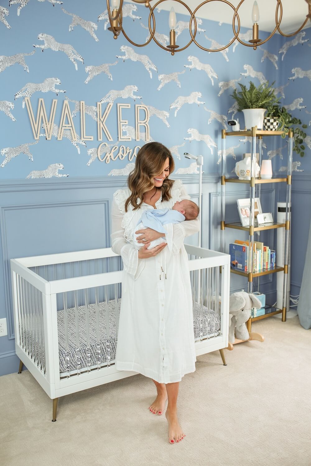 woman in white dress holding newborn in front of white crib