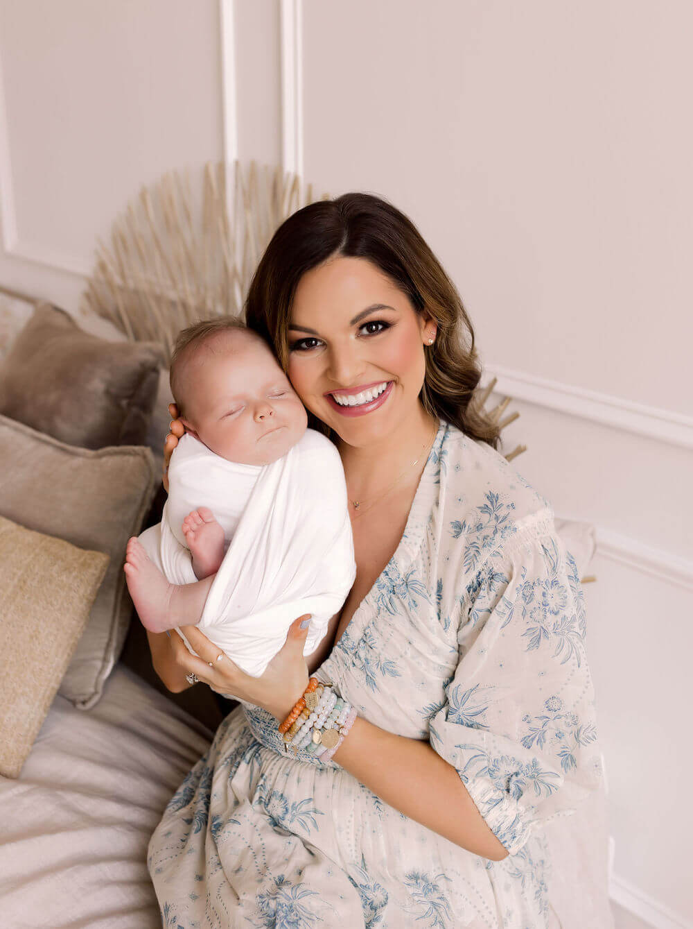 woman in flowy dress holding baby boy in white swaddle