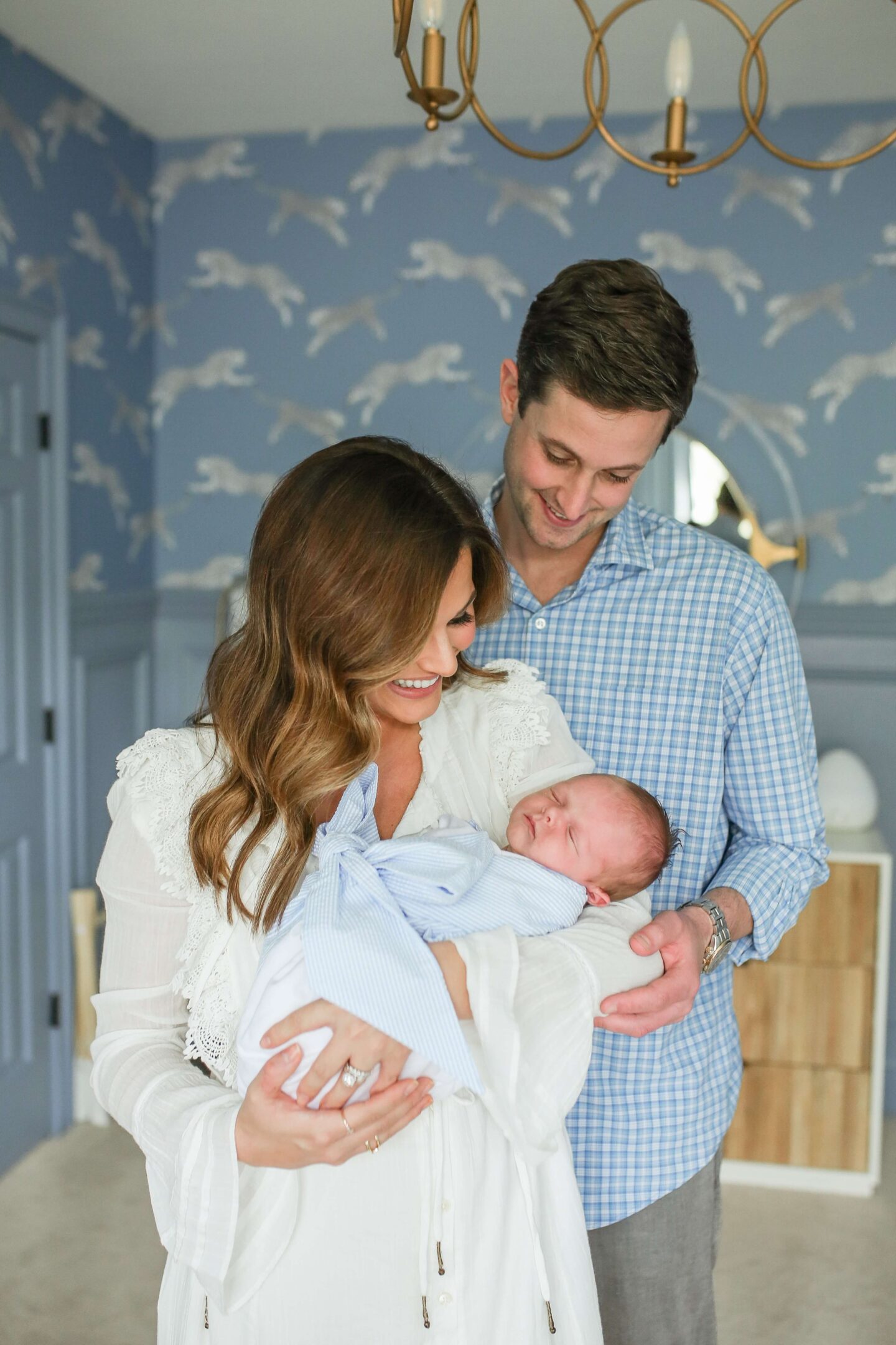 man and woman holding newborn in nursery with little. boy looking down at him