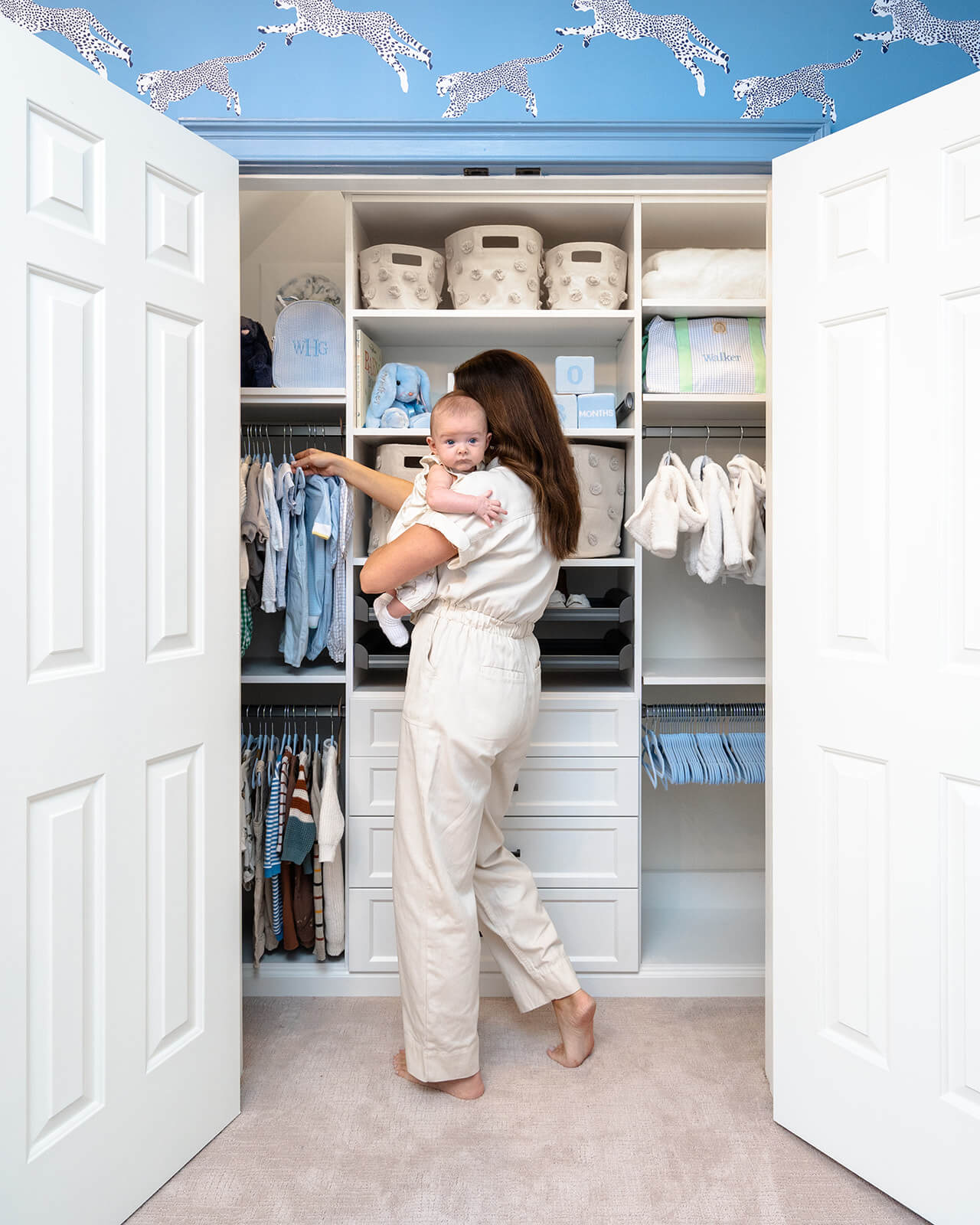woman in tan jumpsuit holding baby boy in front of nursery closet