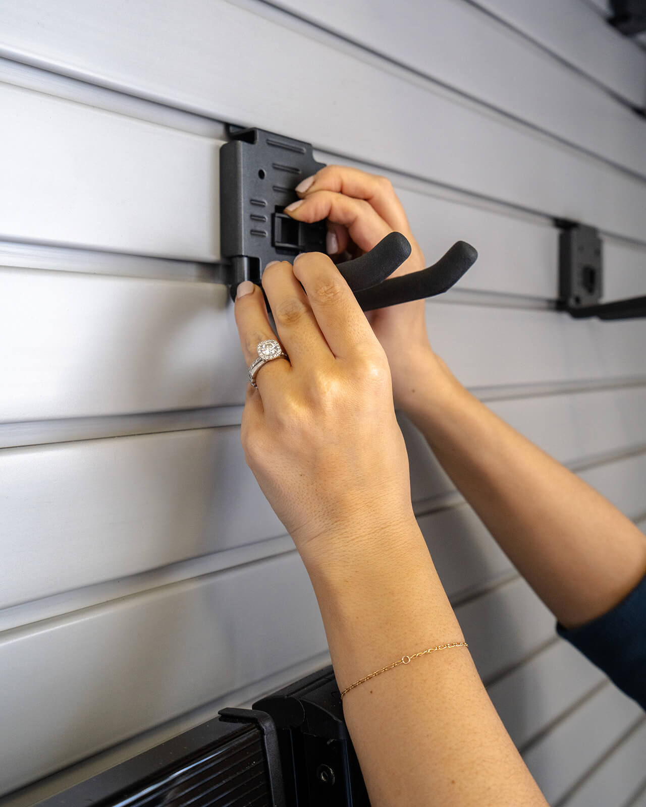 closeup of hands holding hook to hang in slat wall in garage