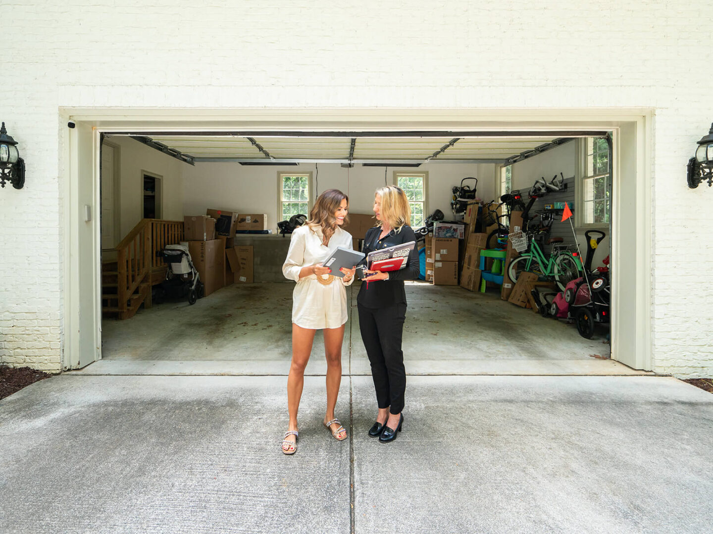 a blonde and brunette woman standing in front of garage planning