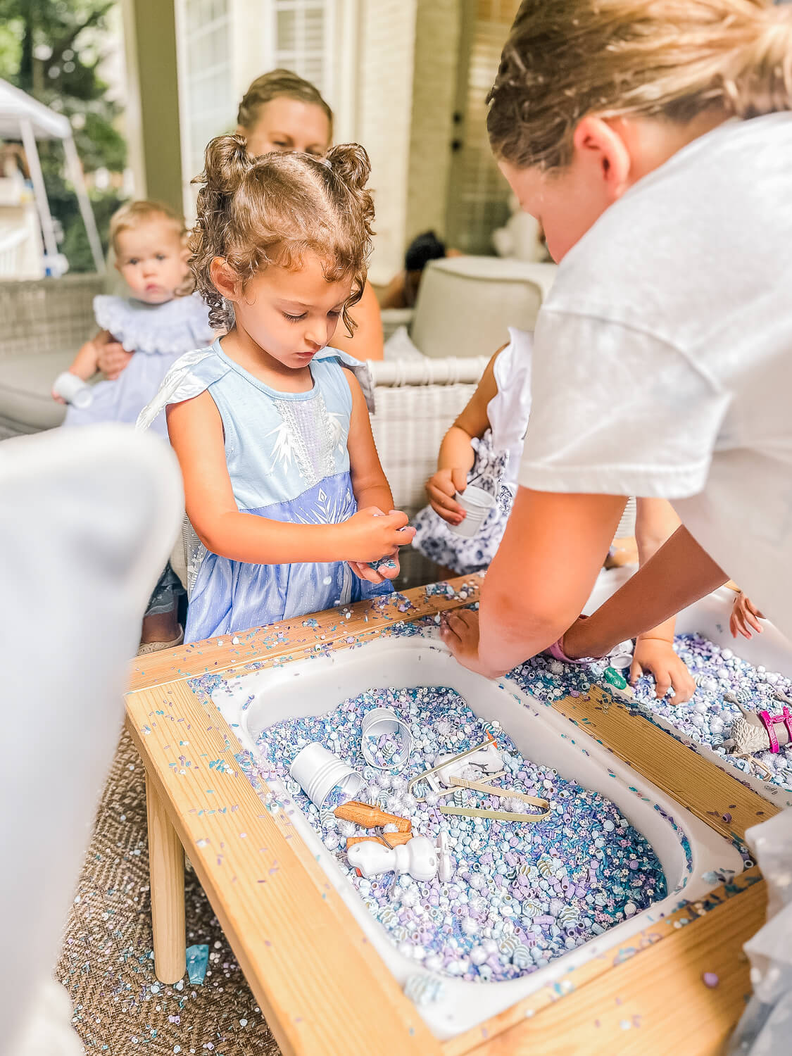 little girl in frozen elsa dress standing at a frozen sensory table