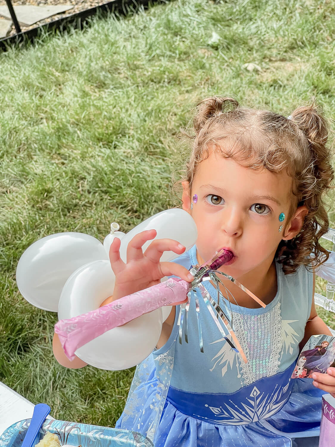 little girl with curly hair blowing a birthday party blower