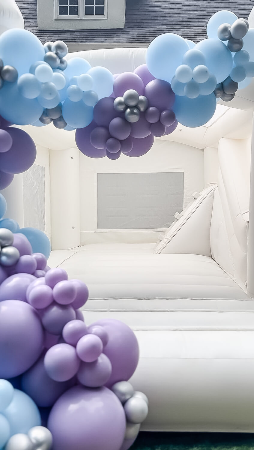 white bouncy castle with a slide and balloon arch with blue and purple balloons