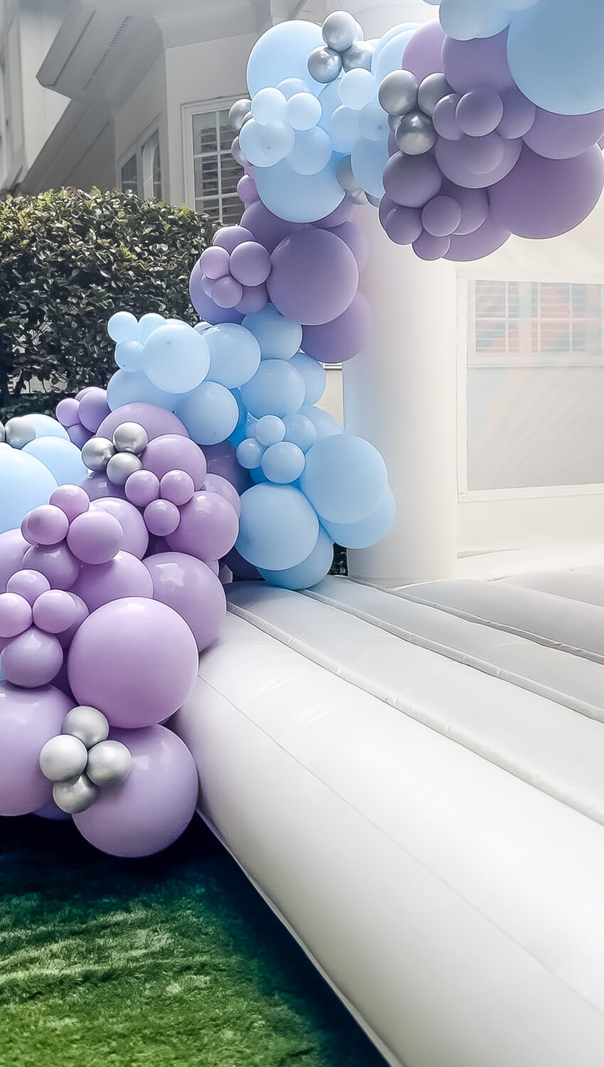 white bouncy castle with balloon arch with blue and purple balloons
