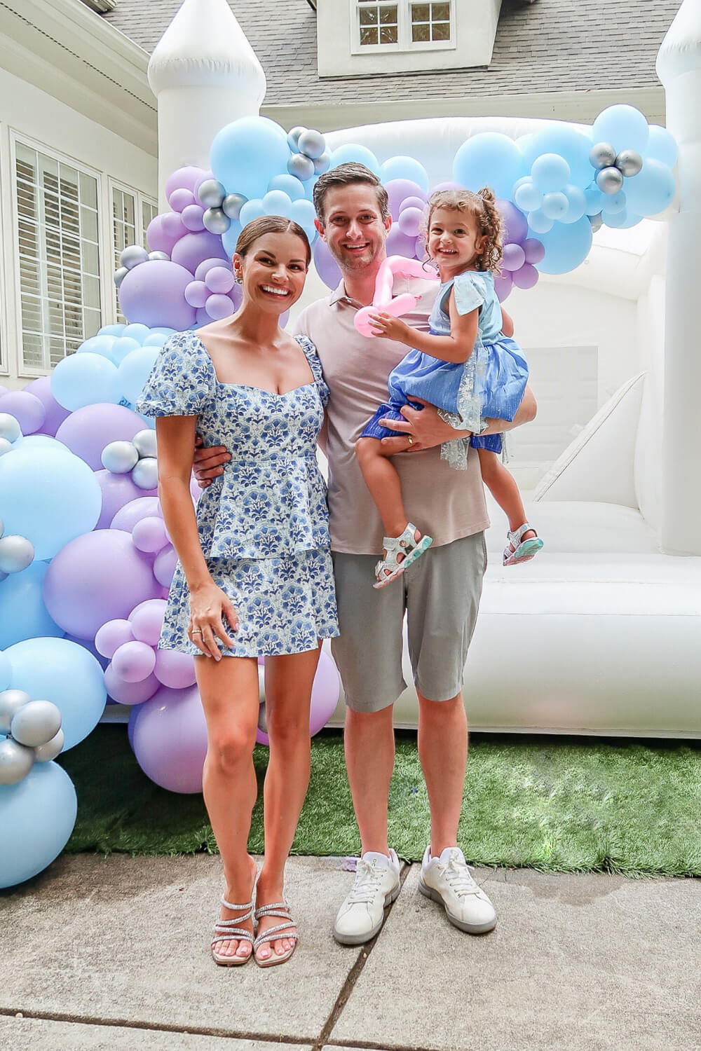 man and woman holding little girl dressed like Elsa in front of white bouncy castle and balloons arch